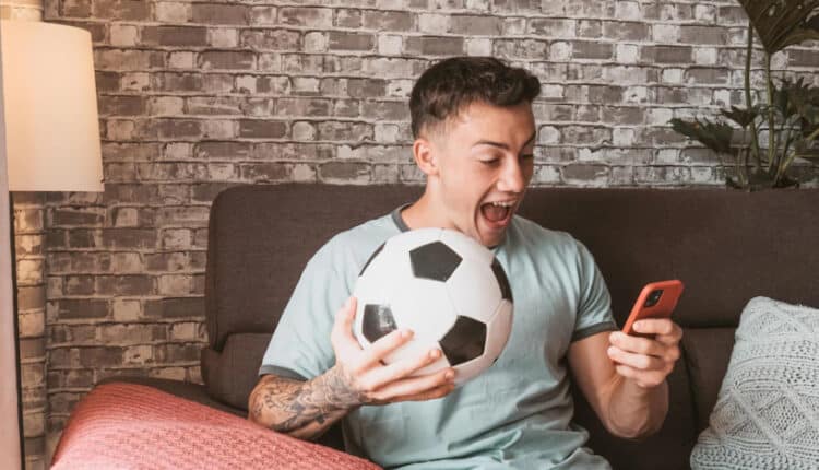 homem segurando uma bola e um celular enquanto aposta online de forma responsável